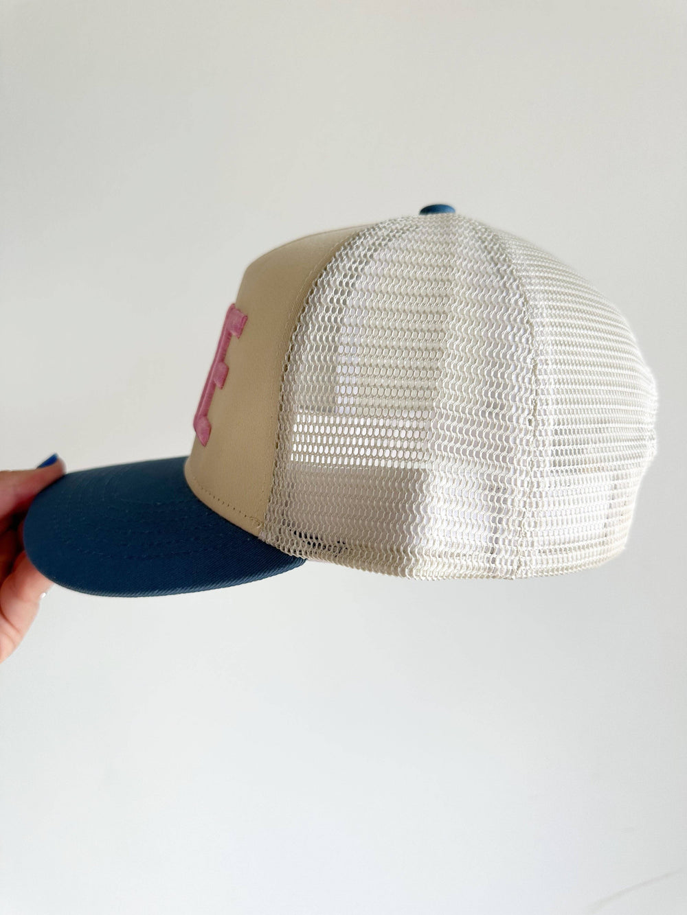 Beige and blue cap with mesh back held against a light gray background